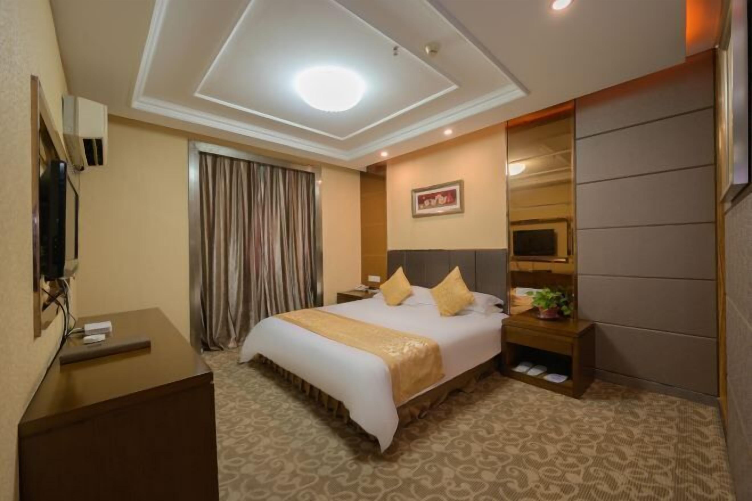 A hotel room with a large bed, a desk, a television, a mirror, and a window with curtains.