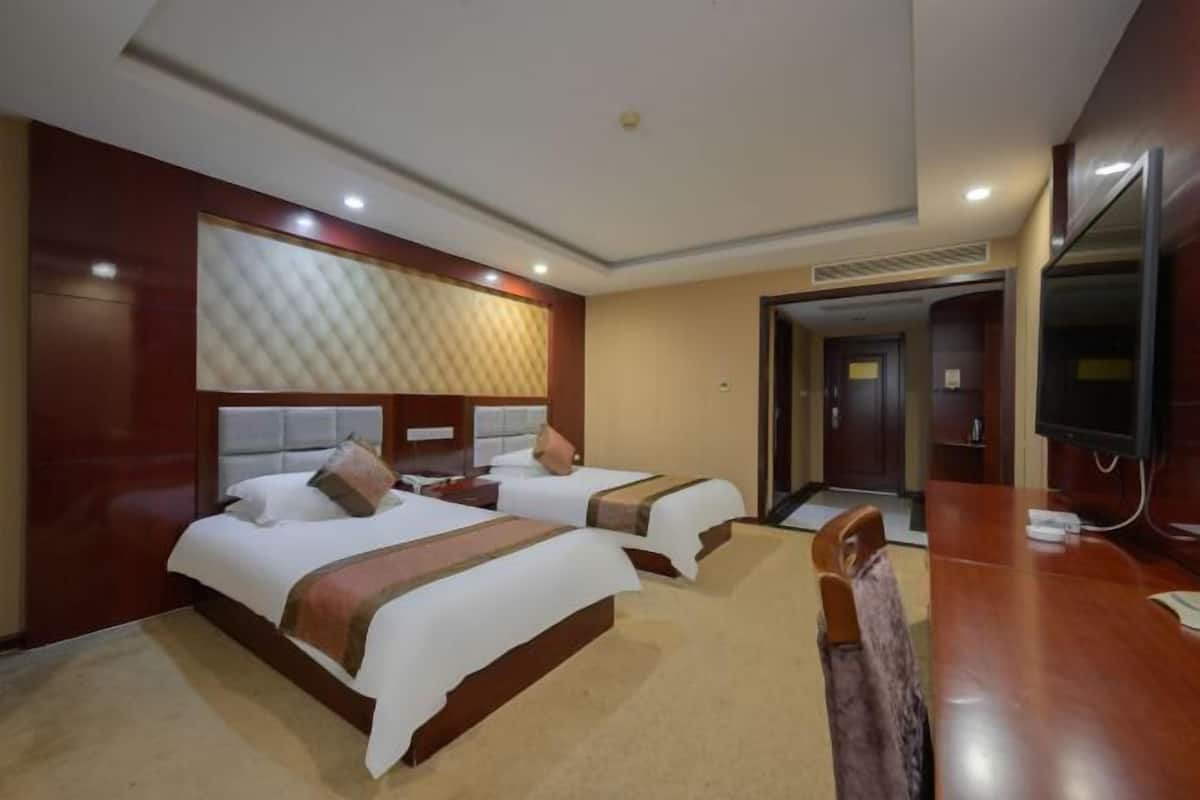 A hotel room with two beds, a wooden headboard, a flat-screen TV, and a desk with a chair.