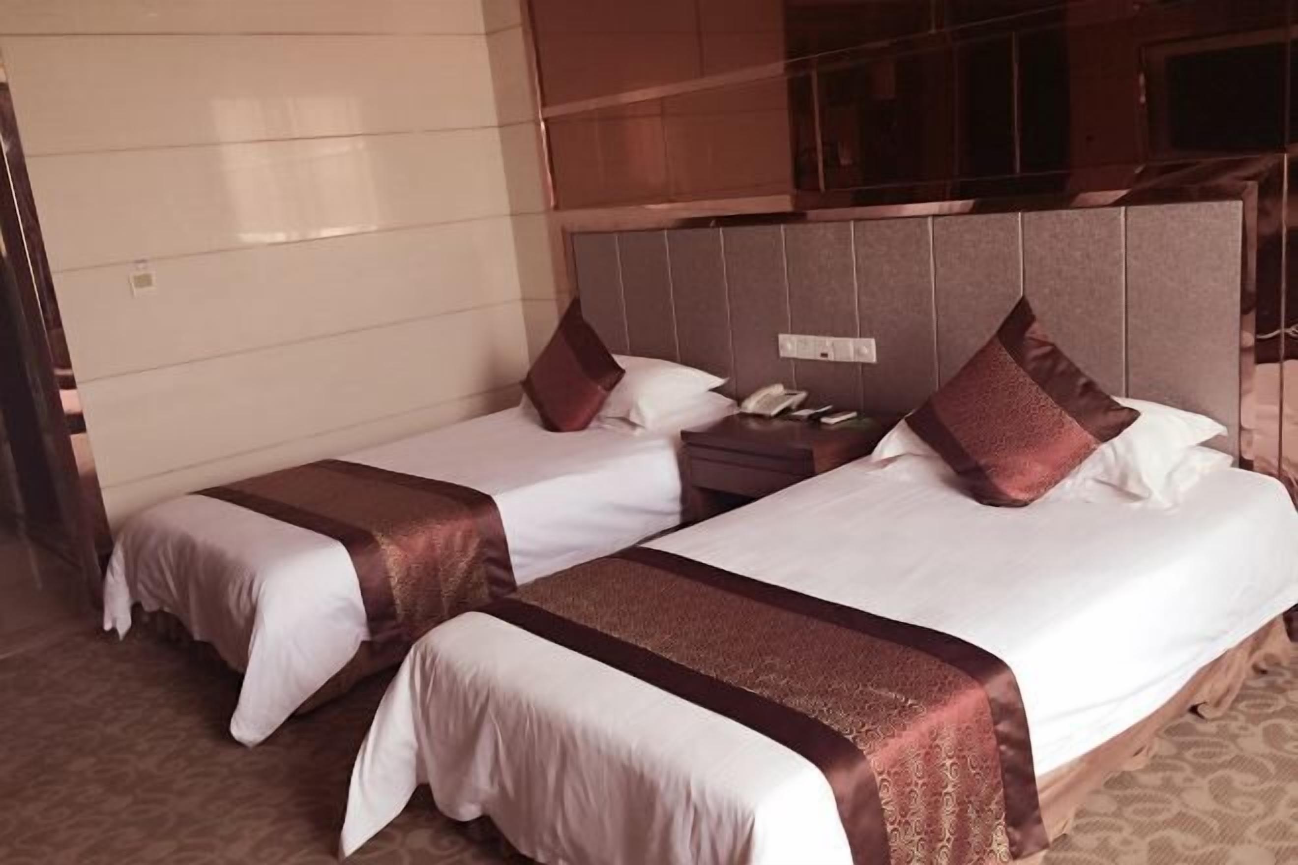 Une chambre d’hôtel avec deux lits, chacun recouvert d’une couverture marron et doté d’oreillers, une table de chevet avec un téléphone et un téléviseur fixé au mur.