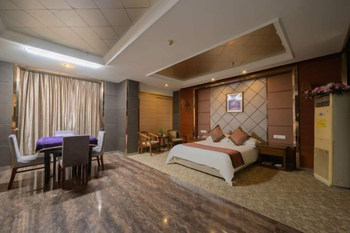 A hotel room with a bed, a dining table with chairs, a small table with a chair, and a refrigerator.