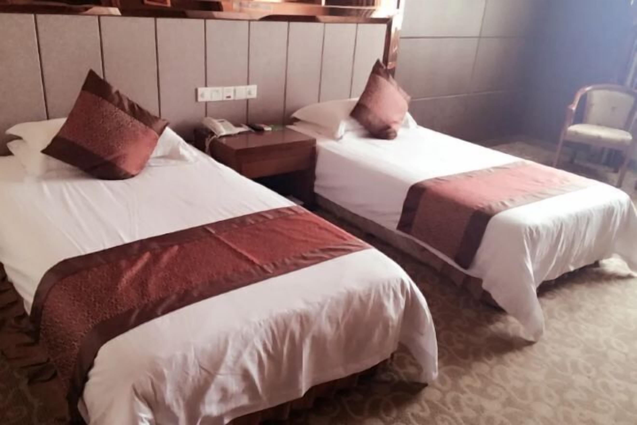 A hotel room with two beds, each with a pillow and a nightstand with a phone.