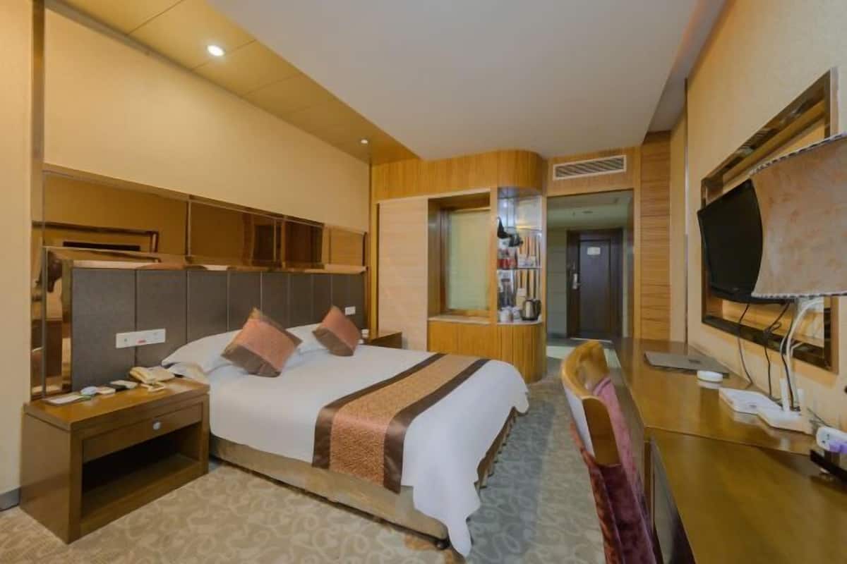 A hotel room with a large bed, a desk with a chair, a television, and a mirror.