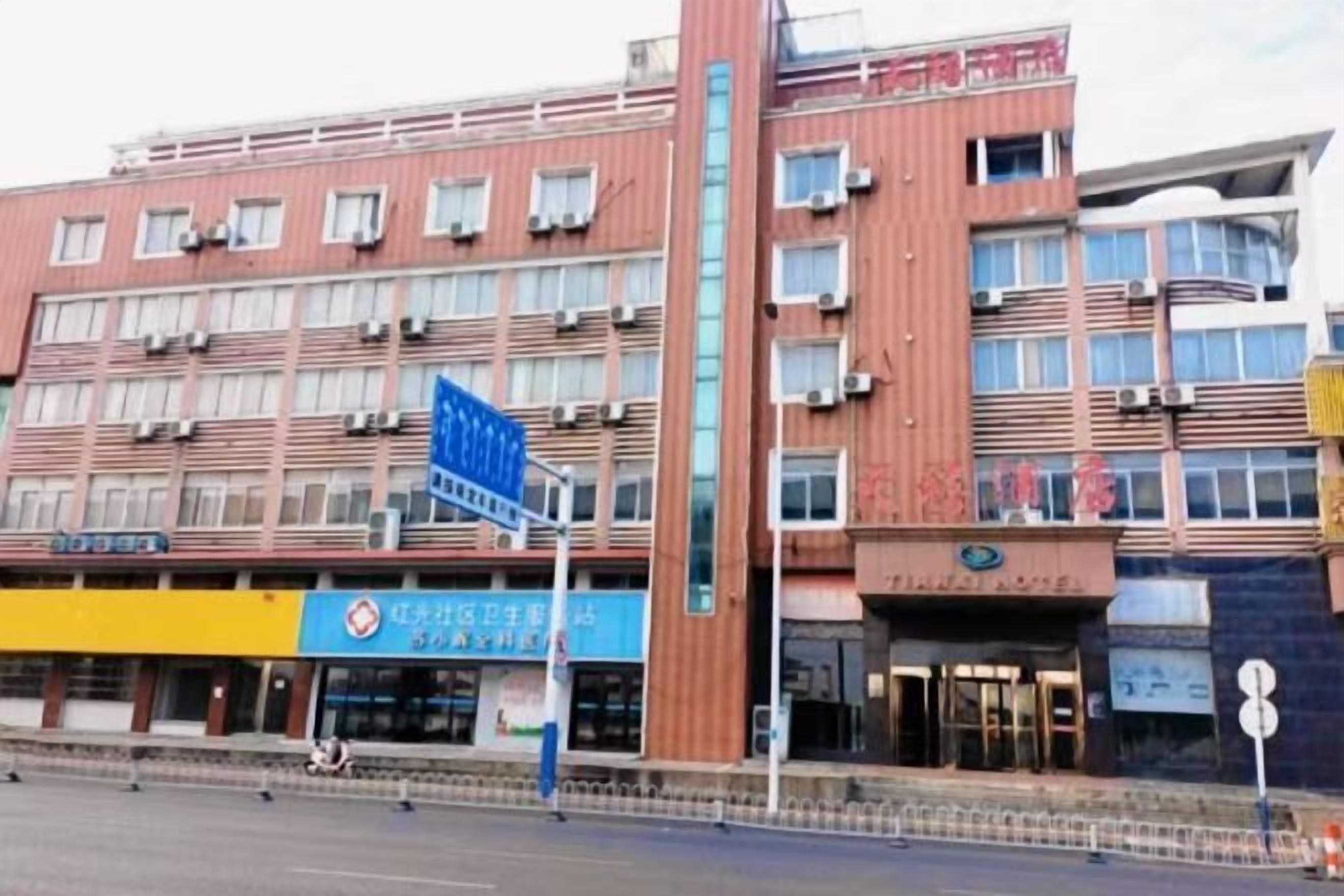 A multi-story hotel with a red facade and multiple air conditioning units. There are signs for a restaurant and a hotel on the ground floor.