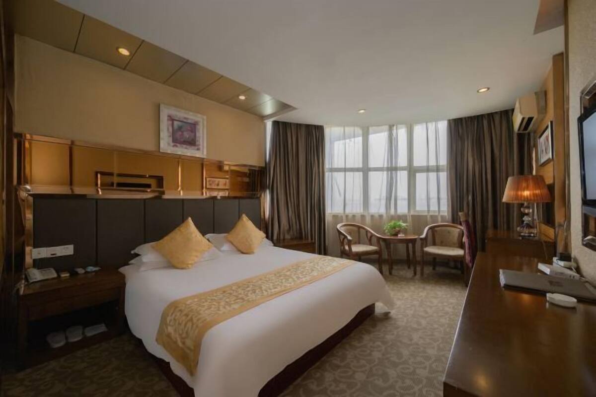 A hotel room with a large bed, a desk, a chair, and a TV.
