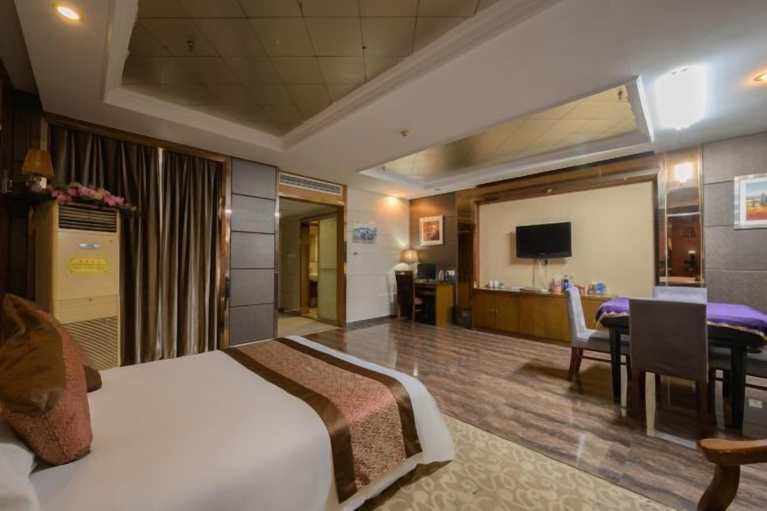 A hotel room with a bed, a desk, a chair, a television, and a reception desk.