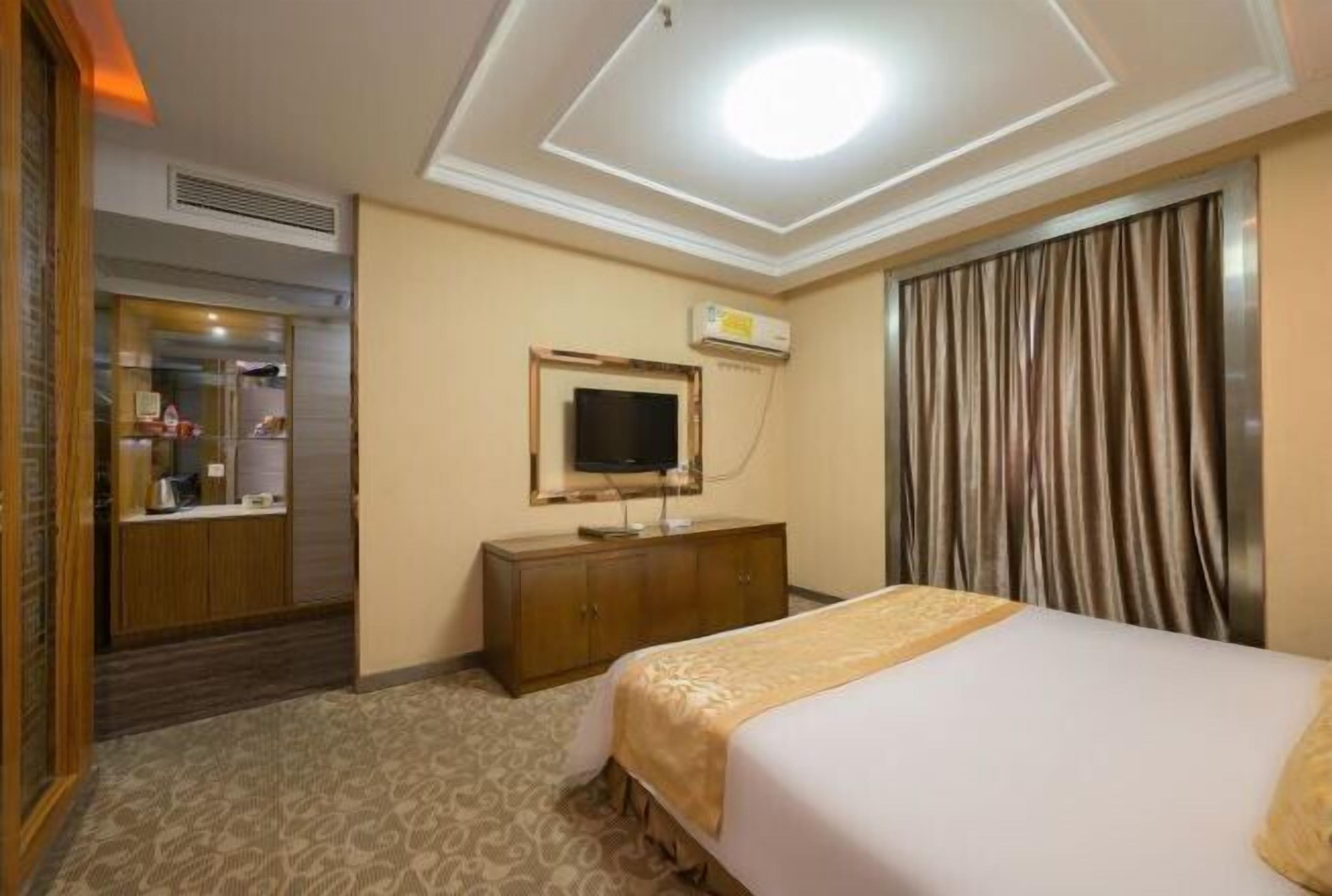 A hotel room with a bed, a dresser, a television, and an air conditioning unit.