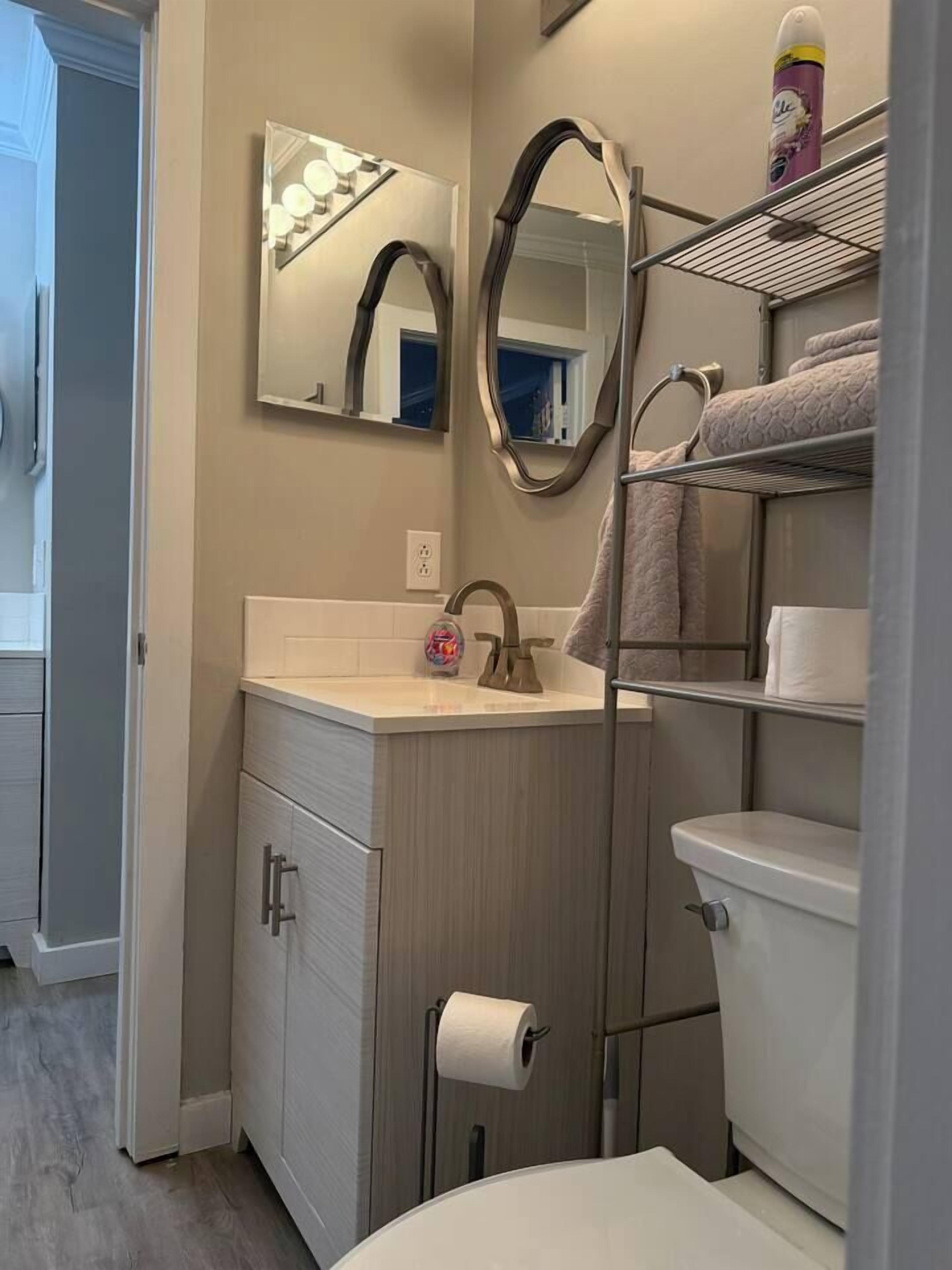 Un bagno con un lavabo, un water, uno scaffale con asciugamani e uno specchio illuminato.