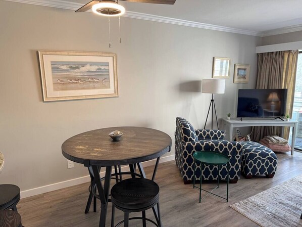 A living room with a round wooden table, patterned sofa, and a television. - Beautiful One Bedroom Retreat (Horry County)