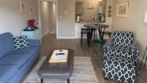 A living room with a sofa, ottoman, and a dining area with a table and chairs.