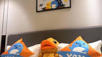 A bed with two pillows featuring a blue and orange duck design, a plush toy duck, and a wall-mounted poster with a cartoon character.