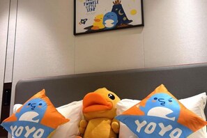 Ein Bett mit zwei Kissen, die ein blaues und oranges Entenmuster zeigen, eine Plüsch-Entenfigur und ein Wandposter mit einer Comicfigur.