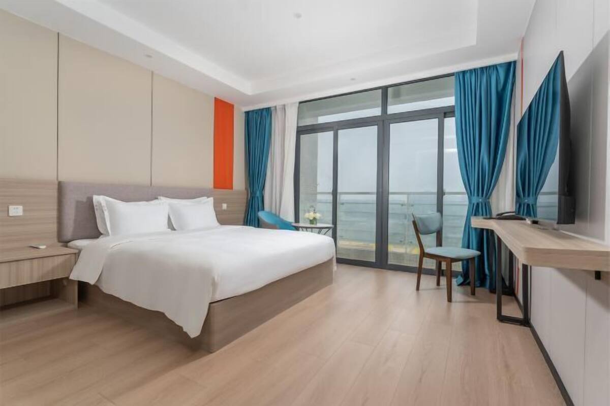 Ein modernes Hotelzimmer mit einem großen Bett, einem Schreibtisch, einem Sessel und einem Fernseher.