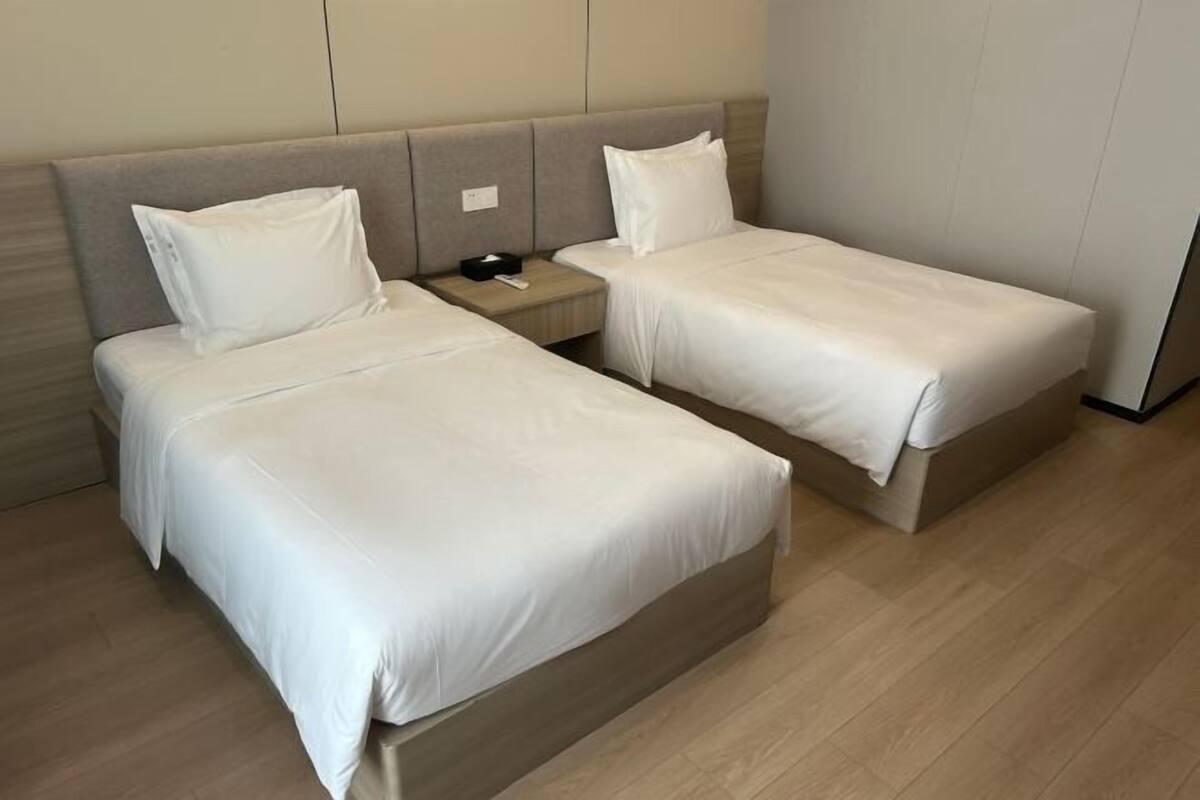Ein Hotelzimmer mit zwei Einzelbetten, einem Nachttisch mit Telefon und einer Schachtel, sowie einem Holzboden.