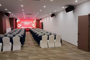 A conference room with rows of tables and chairs, a stage with a red backdrop, and a door on the right. - Xiamen Jingbang Hotel (Xiamen)