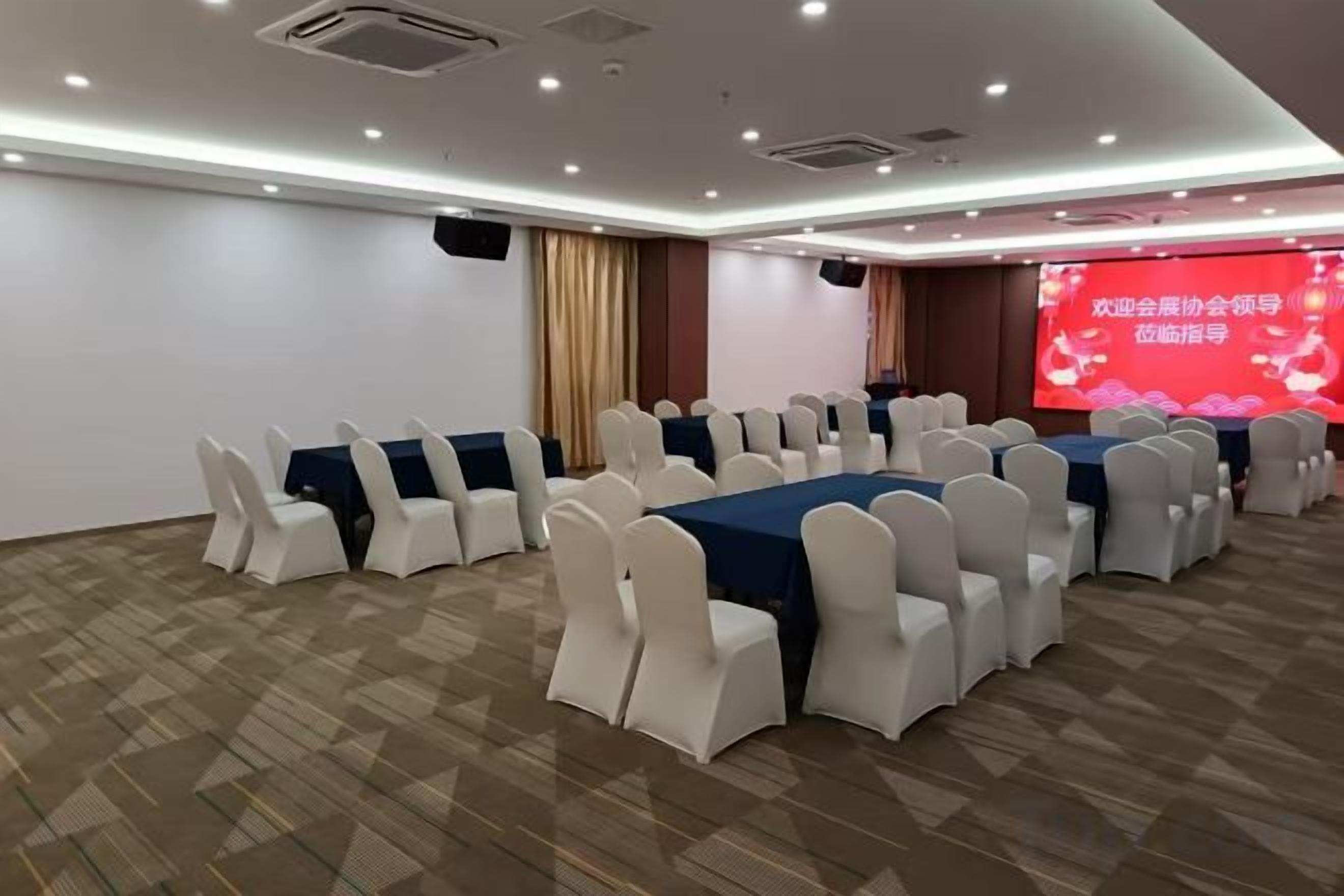 Ein Konferenzraum mit Tischen, Stühlen, einer großen Leinwand und Teppichboden.