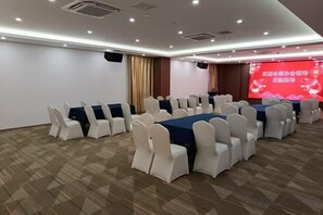 Uma sala de conferências com mesas e cadeiras dispostas em fileiras, uma tela grande e piso coberto de carpete.