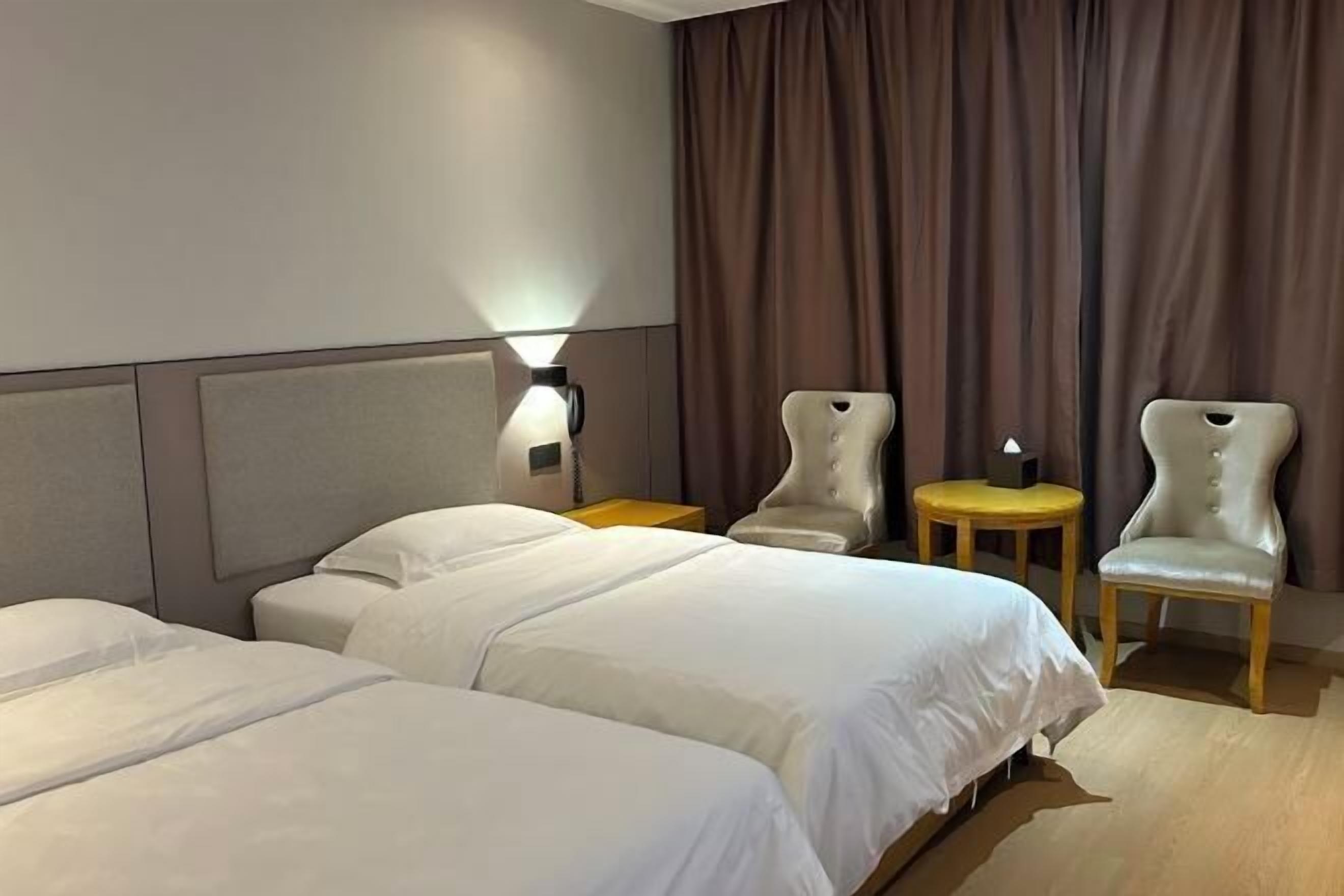 Habitación de hotel con dos camas, una mesita de noche con lámpara, dos sillas y una pequeña mesa.