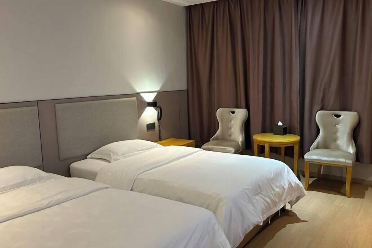 Ein Hotelzimmer mit zwei Betten, einem Nachttisch mit Lampe, zwei Sesseln und einem kleinen Tisch.