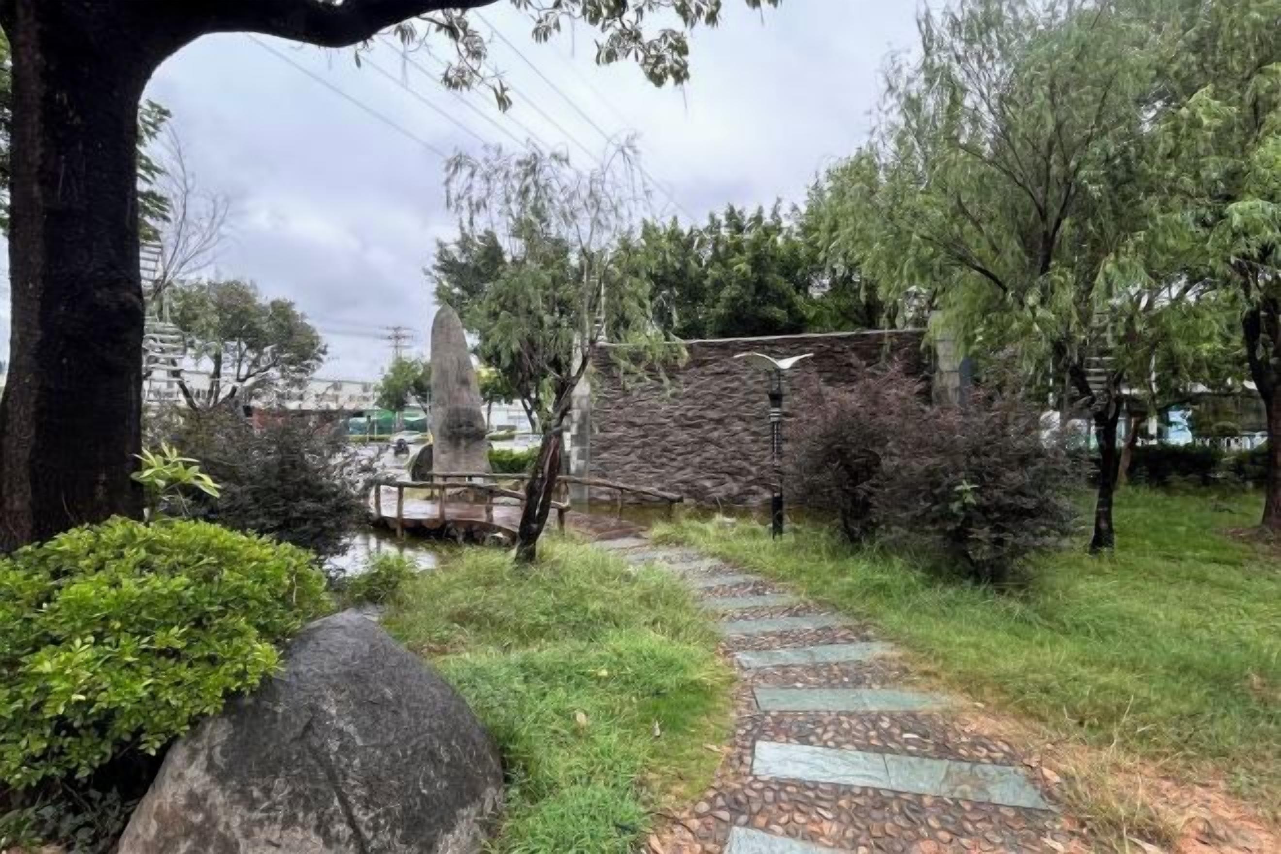 A stone pathway leading through a park with trees and a stone wall.