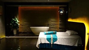 Egy modern fürőszoba, amelyben egy nagy fürdőkád, egy mosdókagyló és egy kék-fehér ágytakaróval borított ágy található.