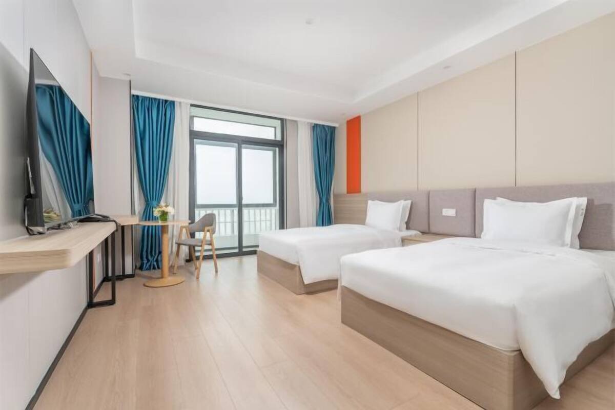 Ein Hotelzimmer mit zwei Betten, einem Schreibtisch, einem Sessel, einem Fernseher und einem großen Fenster mit Vorhängen.