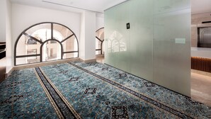 A spacious room with a large, patterned carpet, a glass partition, and a view through arched windows. - Assaafa Golden Hotel  (Madinah)