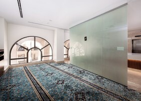A spacious room with a large, patterned carpet, a glass partition, and a view through arched windows.