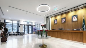 A modern reception area with a round glass table, a reception desk, and framed portraits on the wall. - Assaafa Golden Hotel  (Madinah)