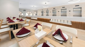 A modern dining area with wooden tables, white chairs, and red napkins. - Assaafa Golden Hotel  (Madinah)