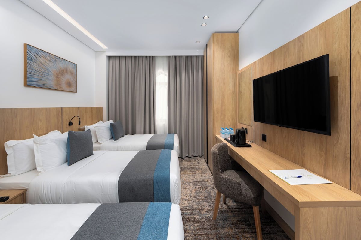 Ett hotellrum med två sängar, ett skrivbord, en TV och ett fönster med gardiner.