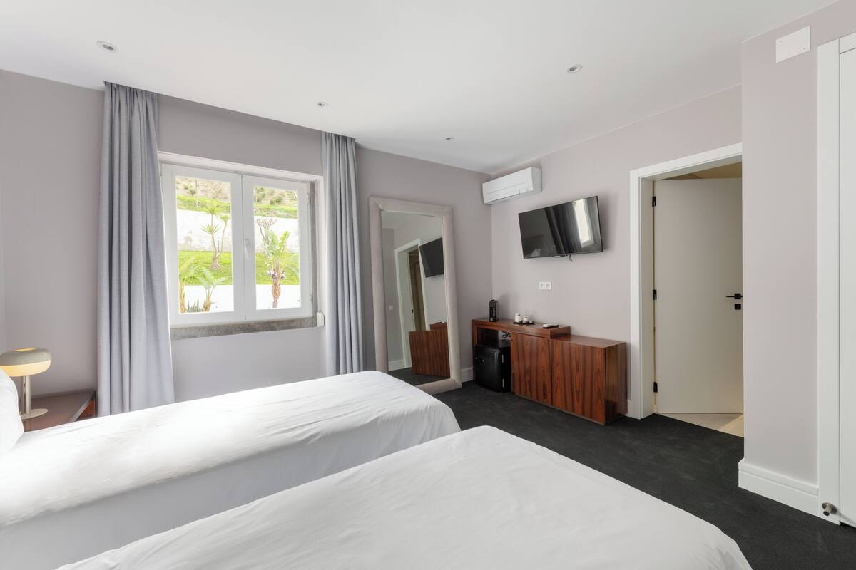 Ein Hotelzimmer mit zwei Betten, einem Schreibtisch, einem Fernseher und Blick auf Grünflächen.
