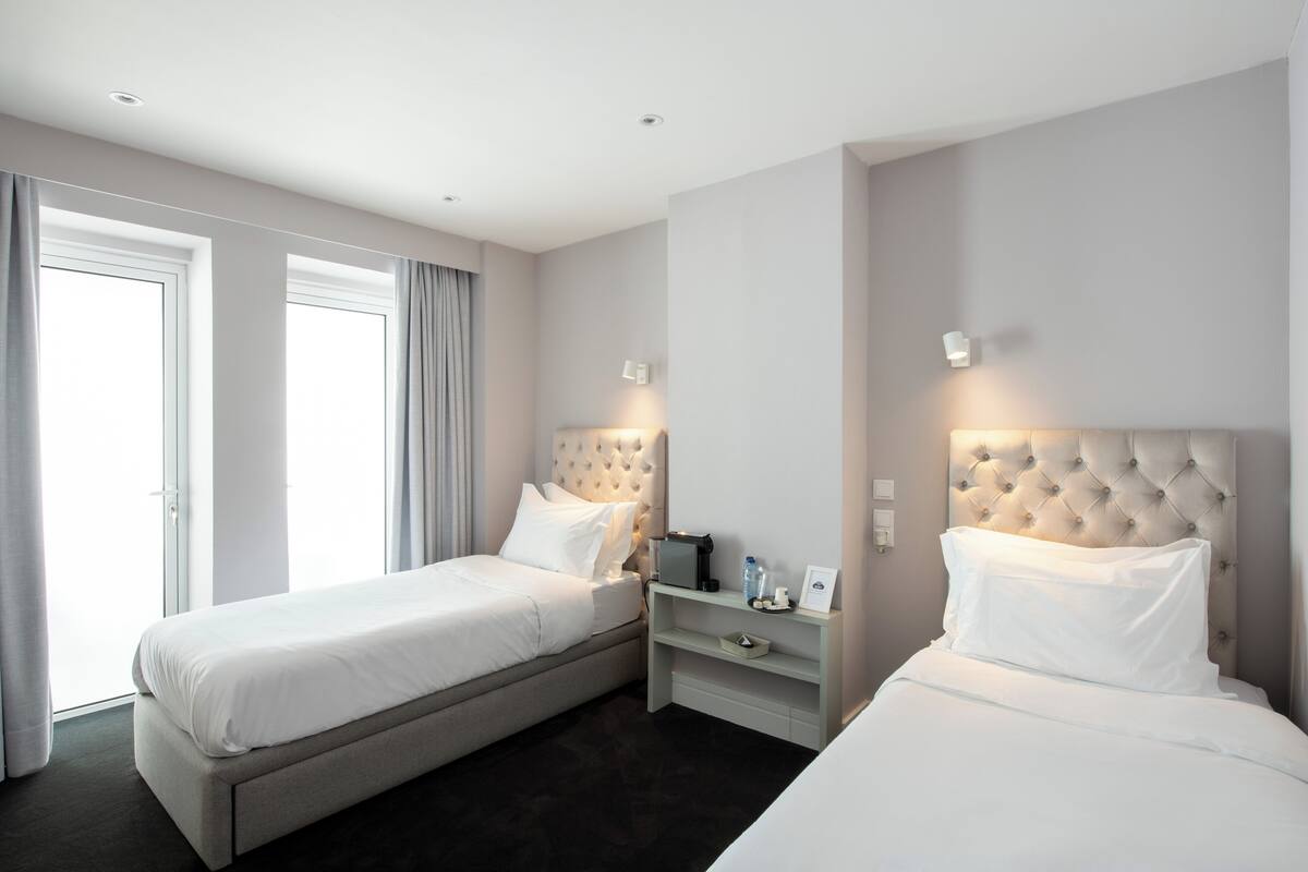 Ein Hotelzimmer mit zwei Betten, einem Nachttisch und einem Fenster mit Vorhängen.