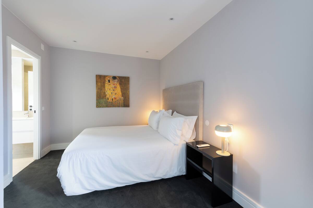 Ein modernes Schlafzimmer mit einem großen Bett, einem Nachttisch mit Lampe und einem Bild an der Wand.