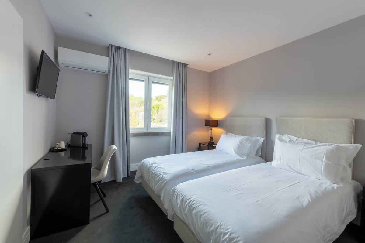 Ein Hotelzimmer mit zwei Betten, einem Schreibtisch, einem Sessel, einem Fernseher und einem Fenster mit Vorhängen.