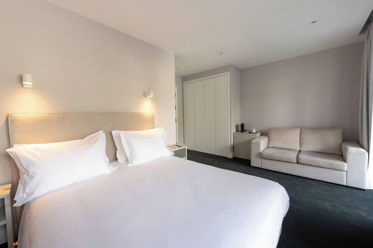 Ein Hotelzimmer mit einem großen Bett, einer Sitzecke und einem Schreibtisch mit Lampe.