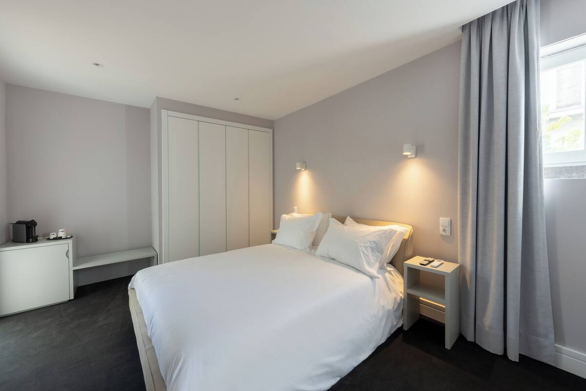 Ein modernes Hotelzimmer mit einem großen Bett, Nachttischen, einem Kleiderschrank und einem Schreibtisch mit Kaffeemaschine.