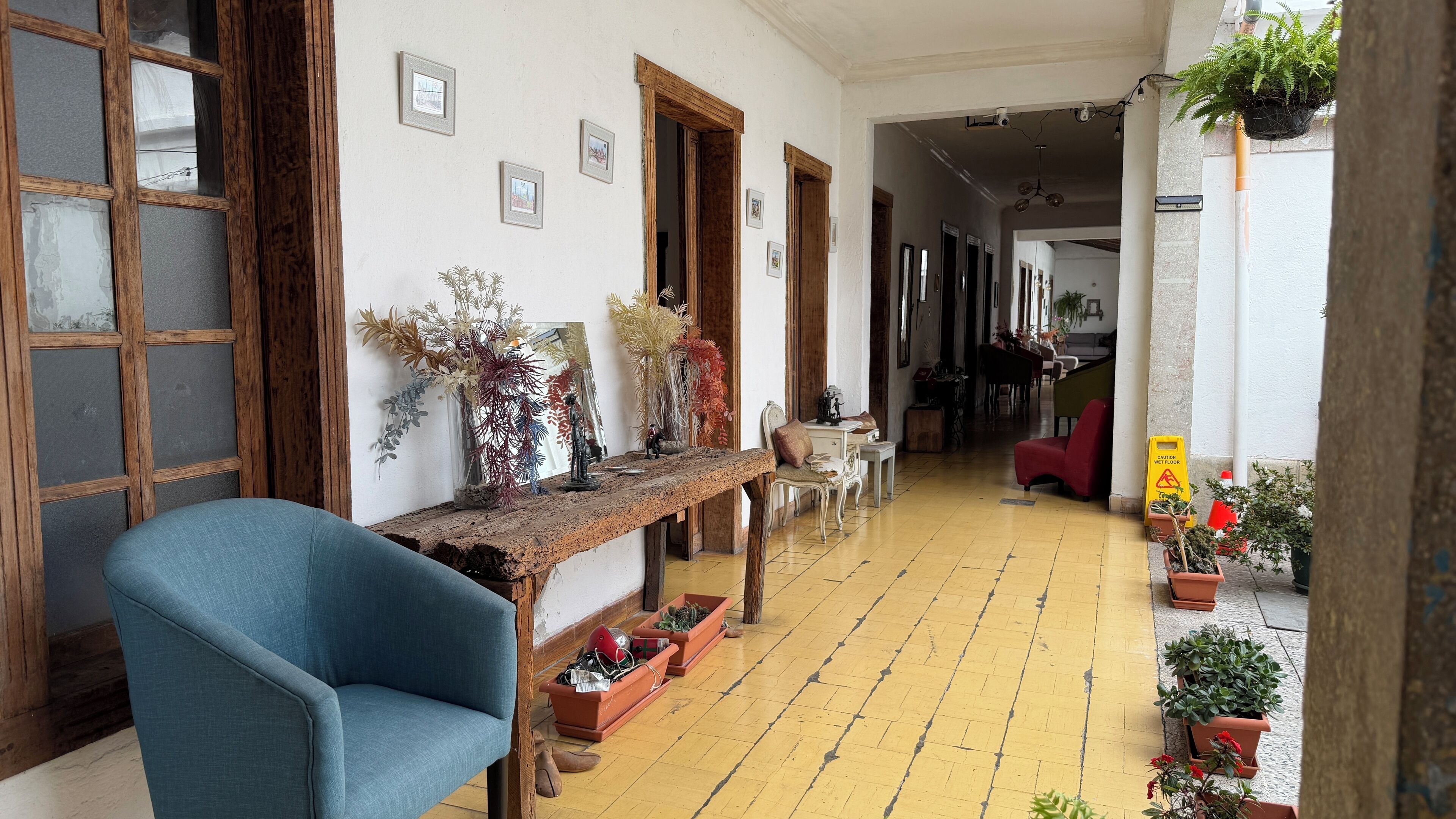 Un couloir avec un banc en bois, des plantes en pot et des tableaux encadrés accrochés aux murs.