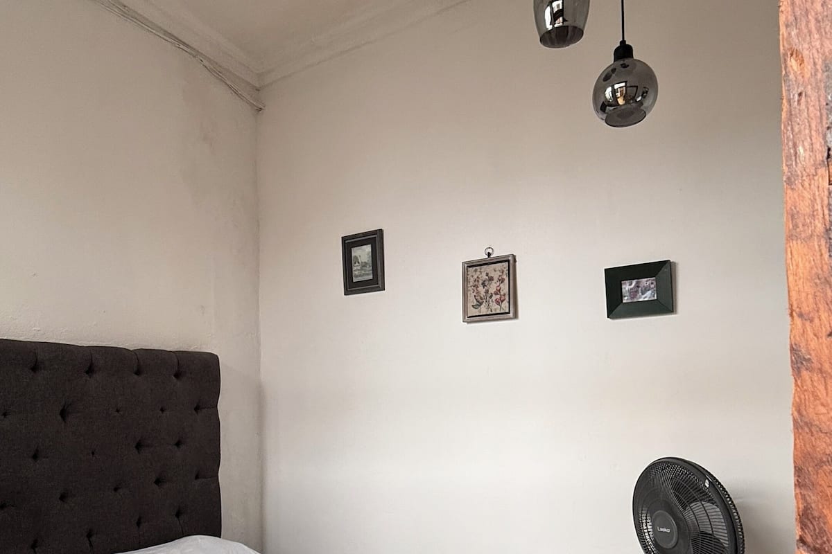 A bedroom with a bed, a blanket, a fan, and three hanging lights.