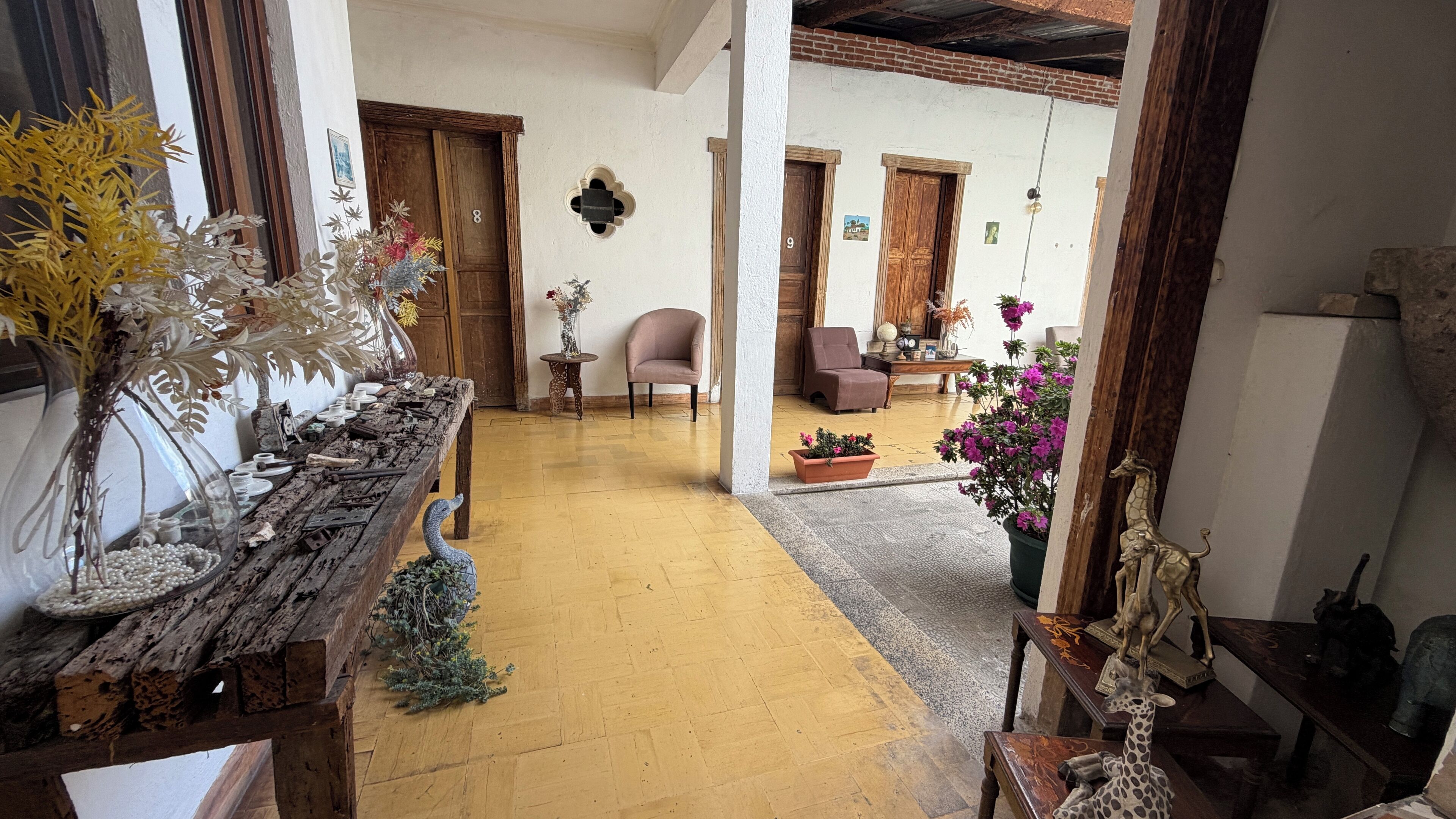 Un pasillo con una mesa de madera rústica, un pequeño árbol de Navidad y una planta en maceta con flores rosadas.