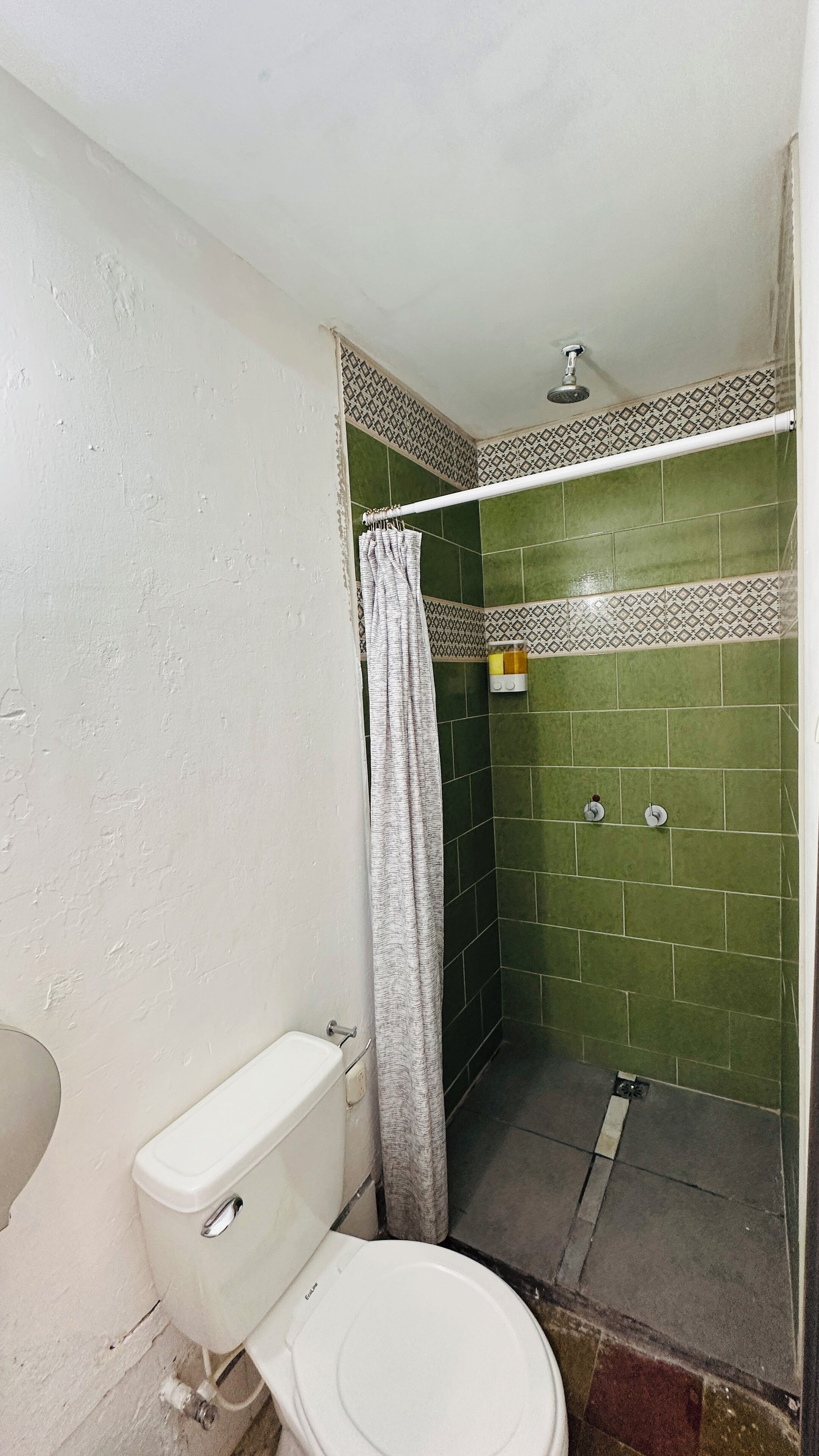 A small bathroom with a white toilet, a shower with green tiles, and a patterned border.