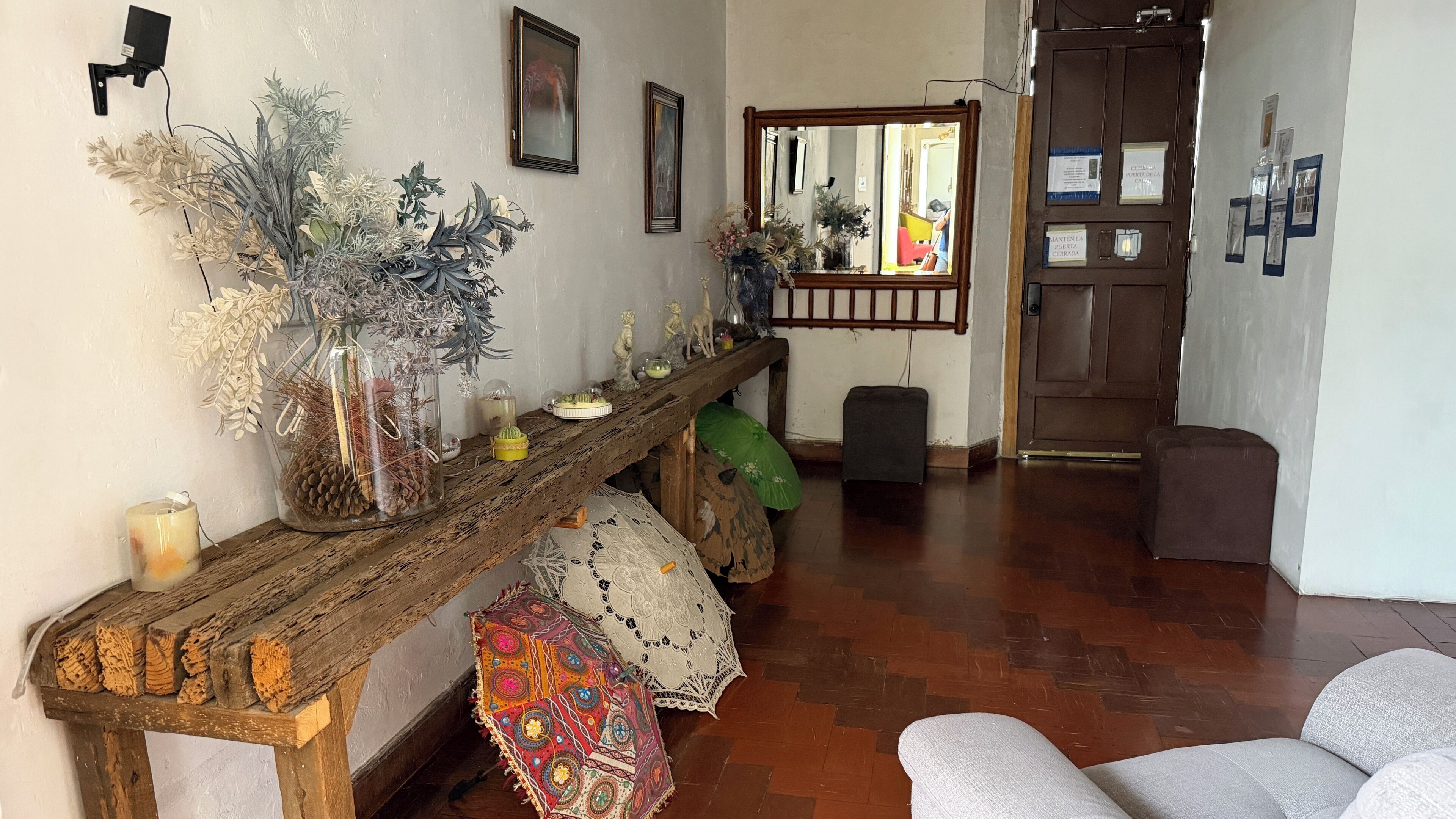 Un pasillo con un banco de madera, un espejo y varios objetos decorativos, entre ellos plantas y una mesita.