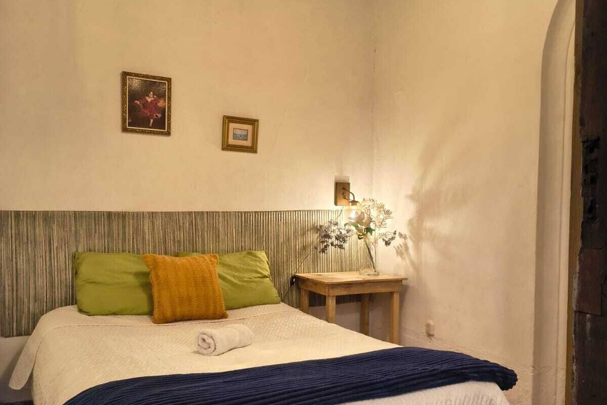 A bedroom with a bed, pillows, a bedside table, and a hanging light fixture.