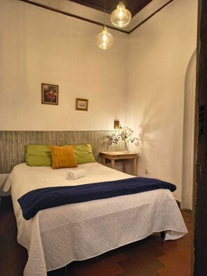 Une chambre à coucher avec un lit, des oreillers, une table de chevet et un luminaire suspendu.