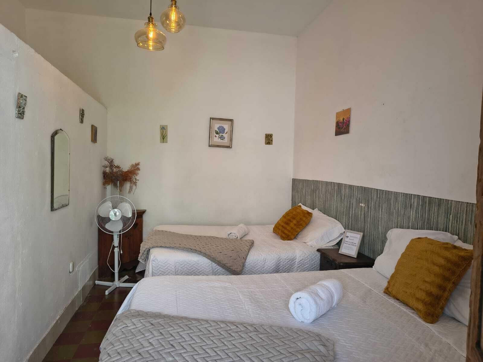 Ein Hotelzimmer mit zwei Betten, einem Standventilator und einem Spiegel.