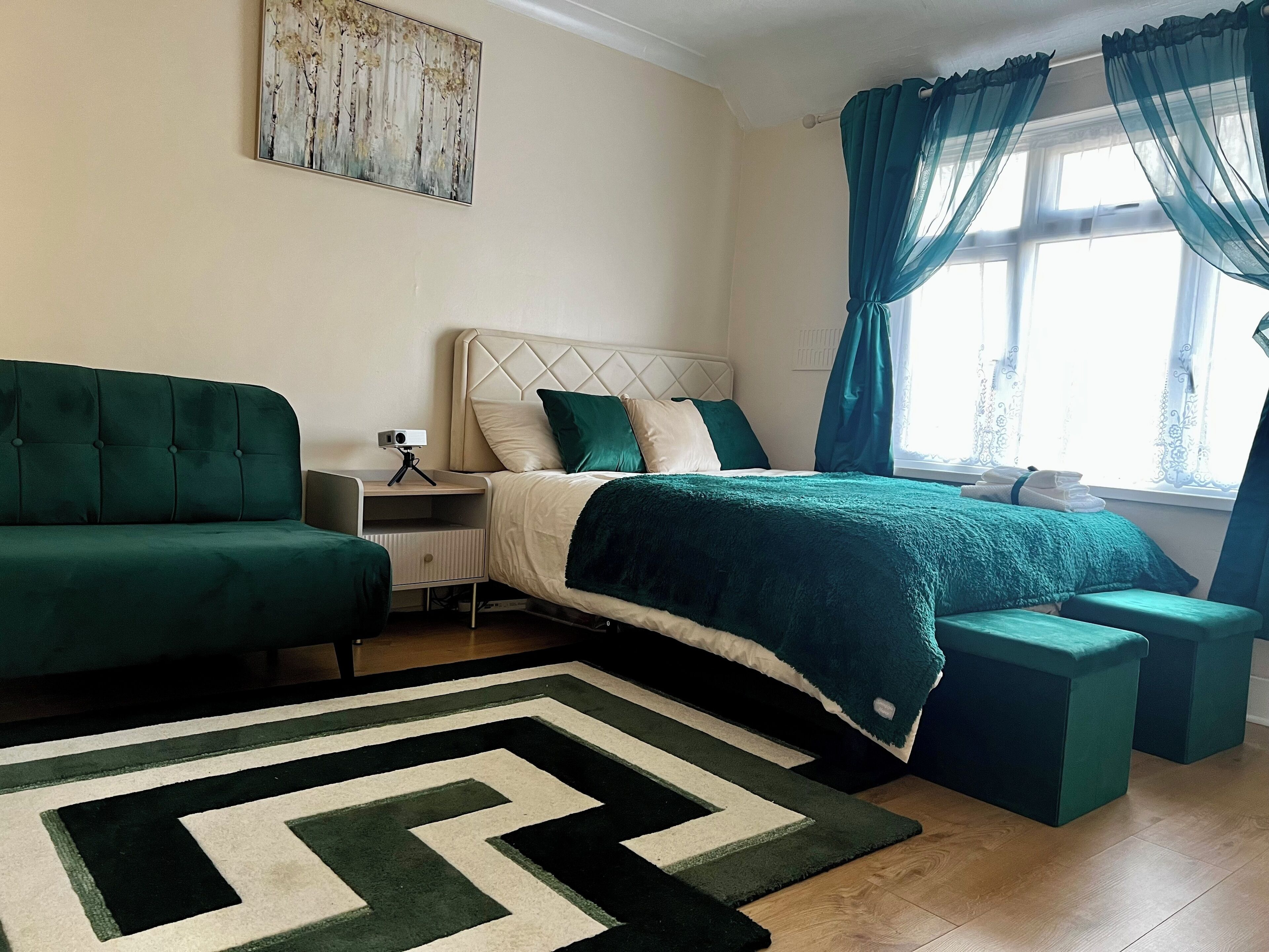 Une chambre à coucher avec un lit, un canapé, une table de chevet, un appareil photo sur un trépied et une fenêtre avec des rideaux.