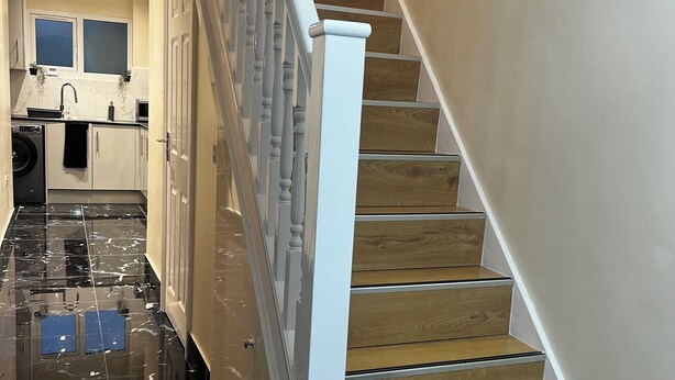 Una escalera con escalones de madera y balaustres blancos que lleva a una zona de desembarco con cocina.