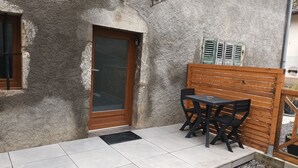 A small outdoor seating area with a table and two chairs, a wooden bench, and a door with a glass panel.