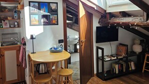 Une cuisine chaleureuse, avec des meubles en bois, un coin repas avec des tabourets, une bibliothèque et un téléviseur fixé au mur.