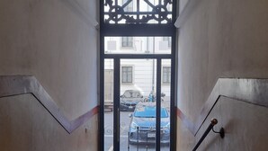 Un escalier menant à une entrée fermée par un portail, d’où l’on peut apercevoir les voitures garées à l’extérieur.