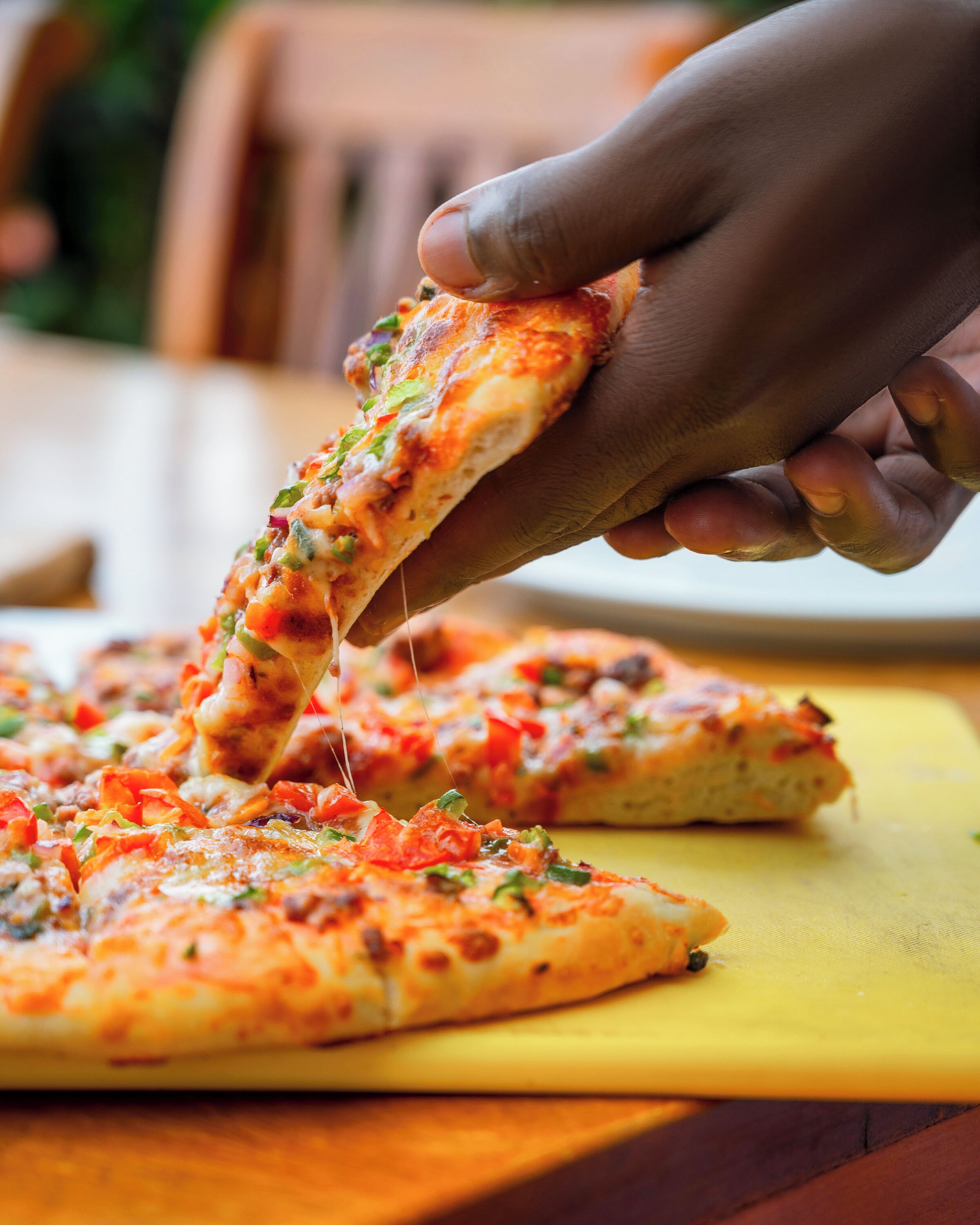 A hand holding a slice of pizza with visible toppings, placed on a yellow surface.